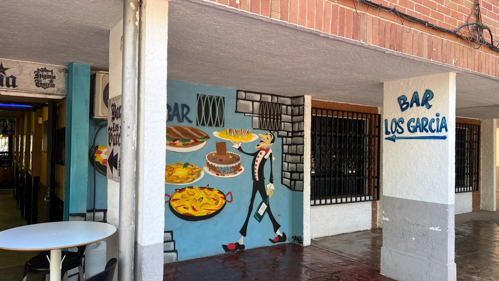 Mural de un camarero con paella y postres en la fachada del Bar Los García.