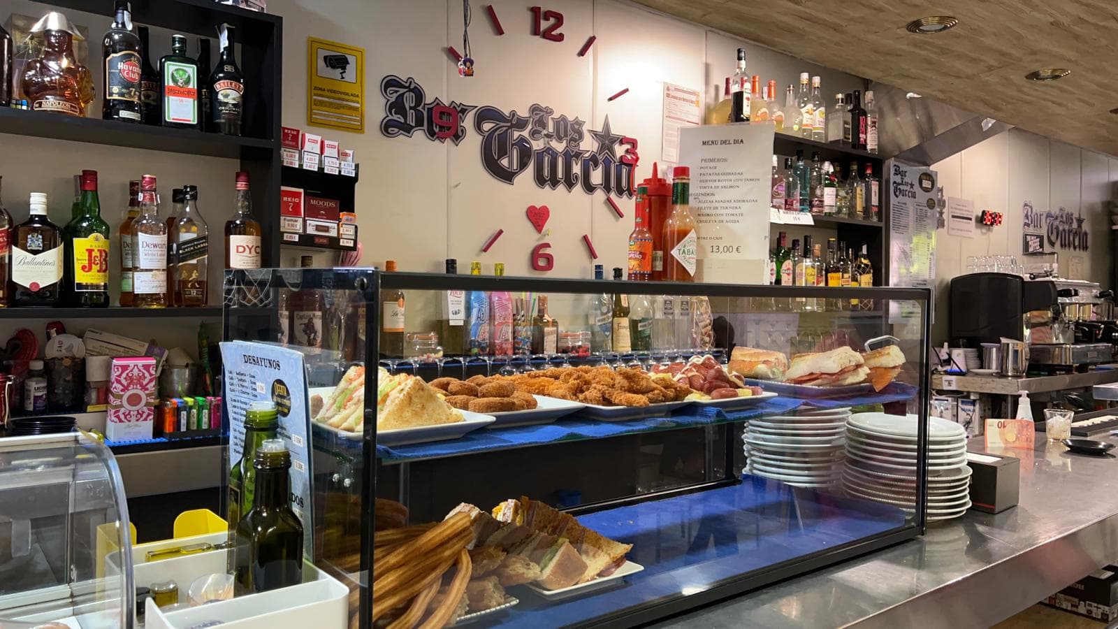 Vitrina de bar con tapas y churros frente a estanterías llenas de botellas de licor.